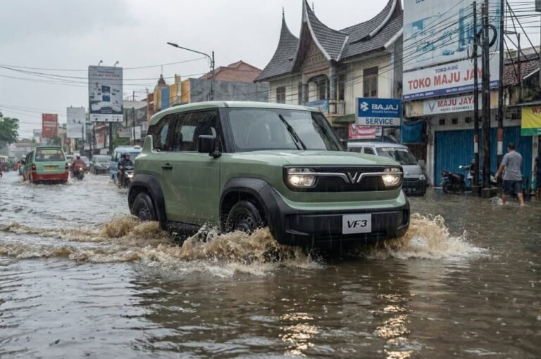 Mobil listrik VinFast VF3 hijau menerobos genangan air banjir di jalan kota yang ramai.