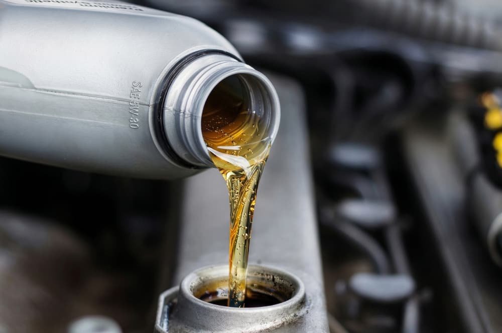 Proses pengisian oli mesin konvensional yang jernih dan berkilau ke dalam tangki kendaraan.